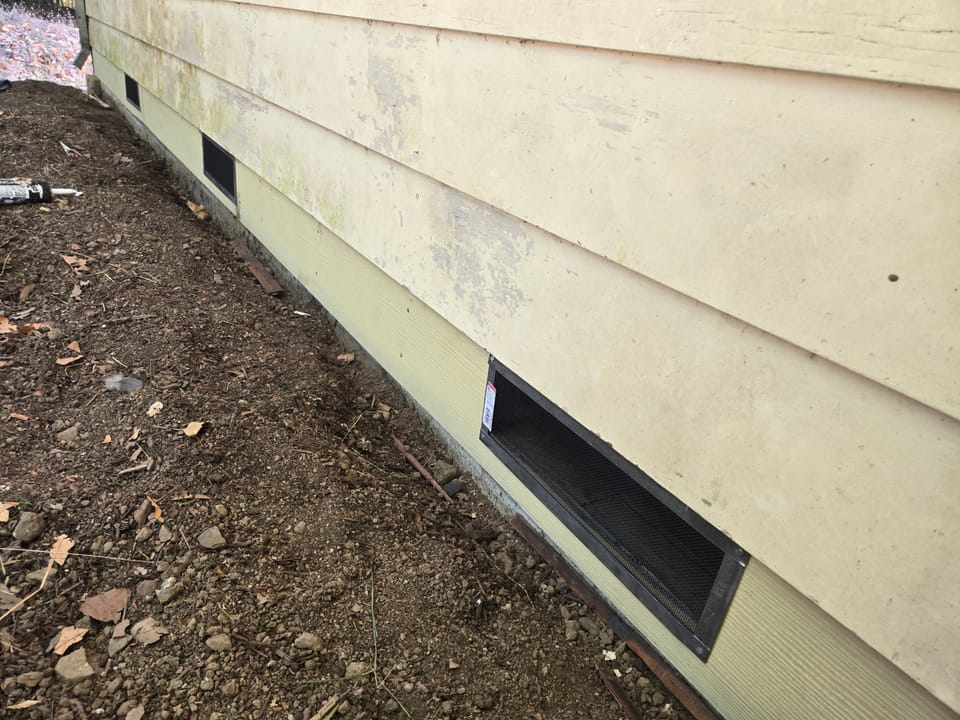 Fine mesh ember-resistant vents installed along the foundation base of a house with horizontal siding.