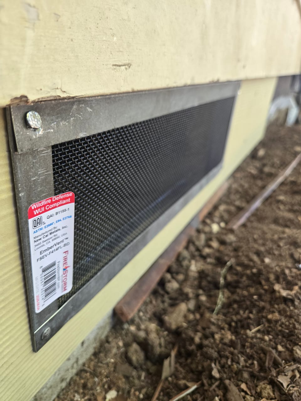 Ember-resistant metal mesh foundation vent installed along the base of home siding.