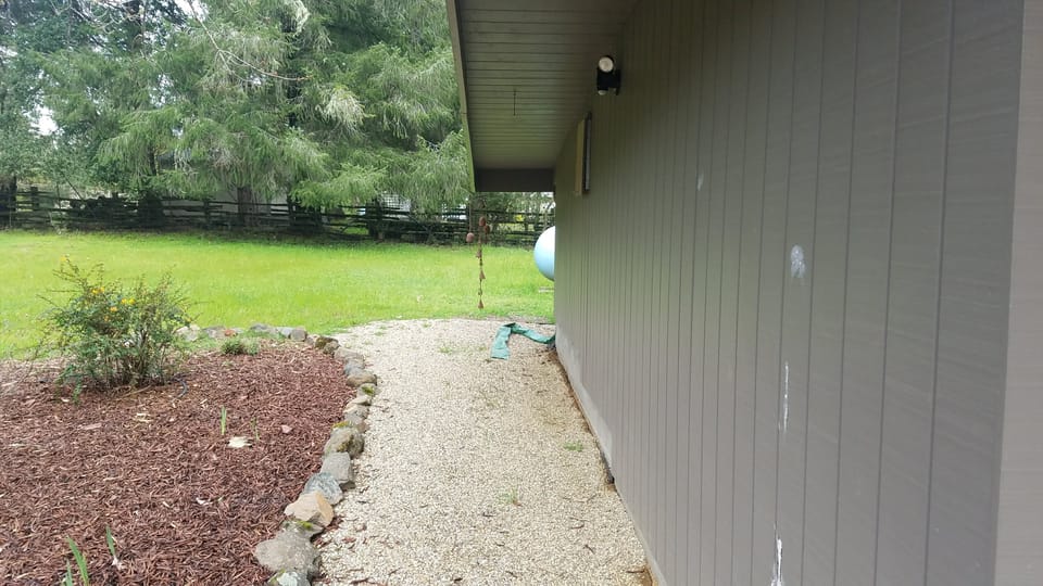 Gravel walkway separating a house wall from a mulched garden bed and green lawn.