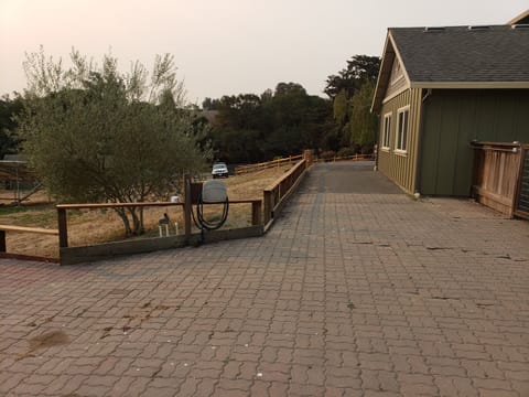 Interlocking paver driveway alongside a green house with a hose reel and smoky skies above.
