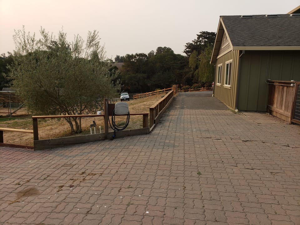 Interlocking paver driveway alongside a green house with a hose reel and smoky skies above.