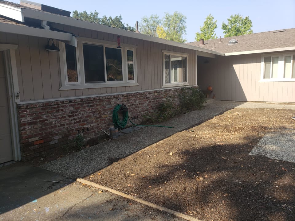 Exterior of a single-story home with brick wainscoting, a concrete walkway, and a bare dirt yard with mulch.