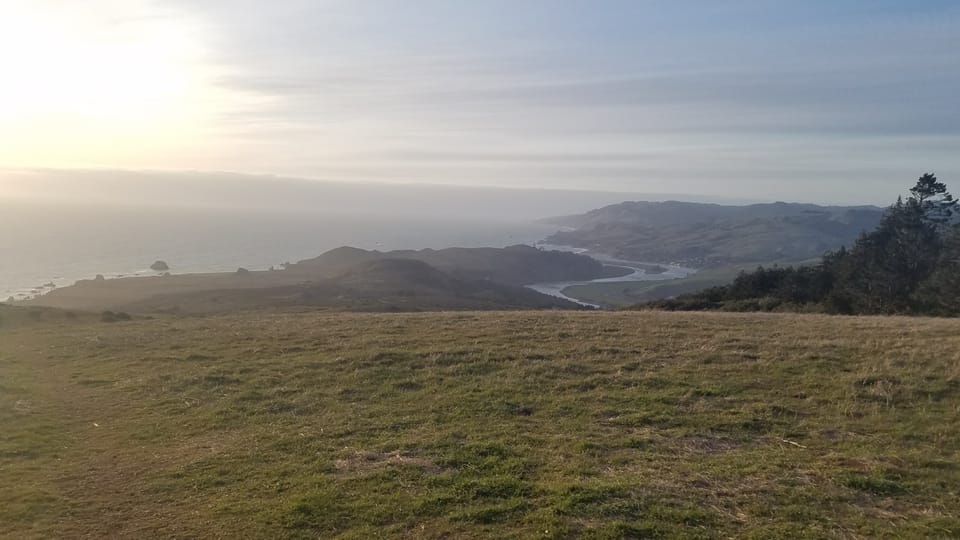 High coastal view over grassy slopes looking down at the Russian River estuary entering the Pacific Ocean.