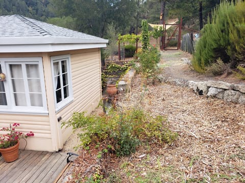 Exterior of a small outbuilding next to a hillside garden path covered in wood chips with stone retaining walls.