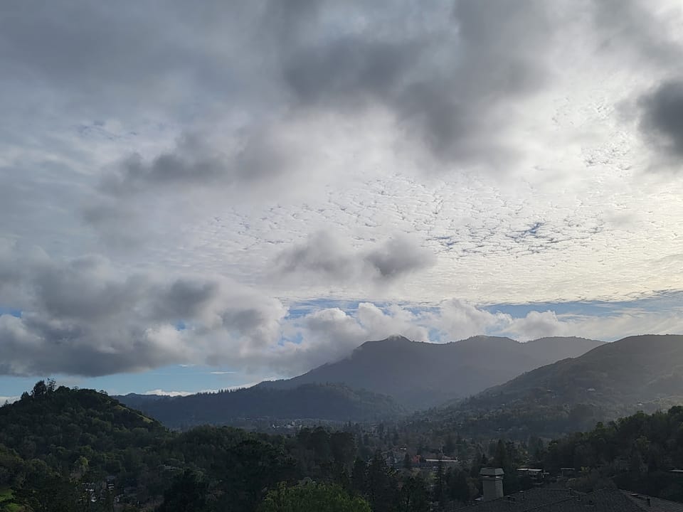 Dark storm clouds gather above a forested mountain ridge and wooded valley.