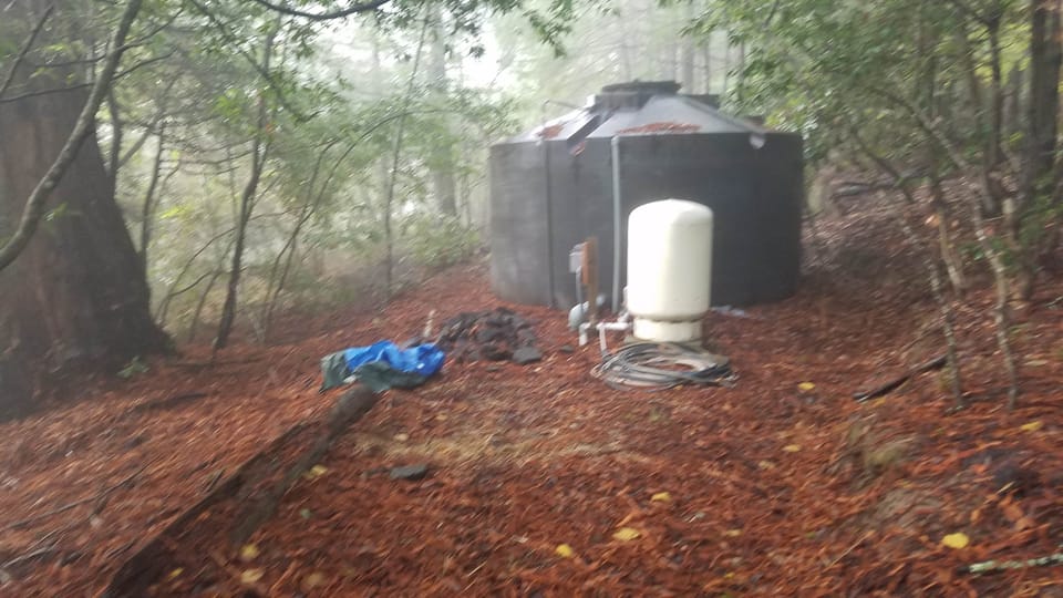 Large dark water storage tank and white pressure tank in a foggy redwood forest.